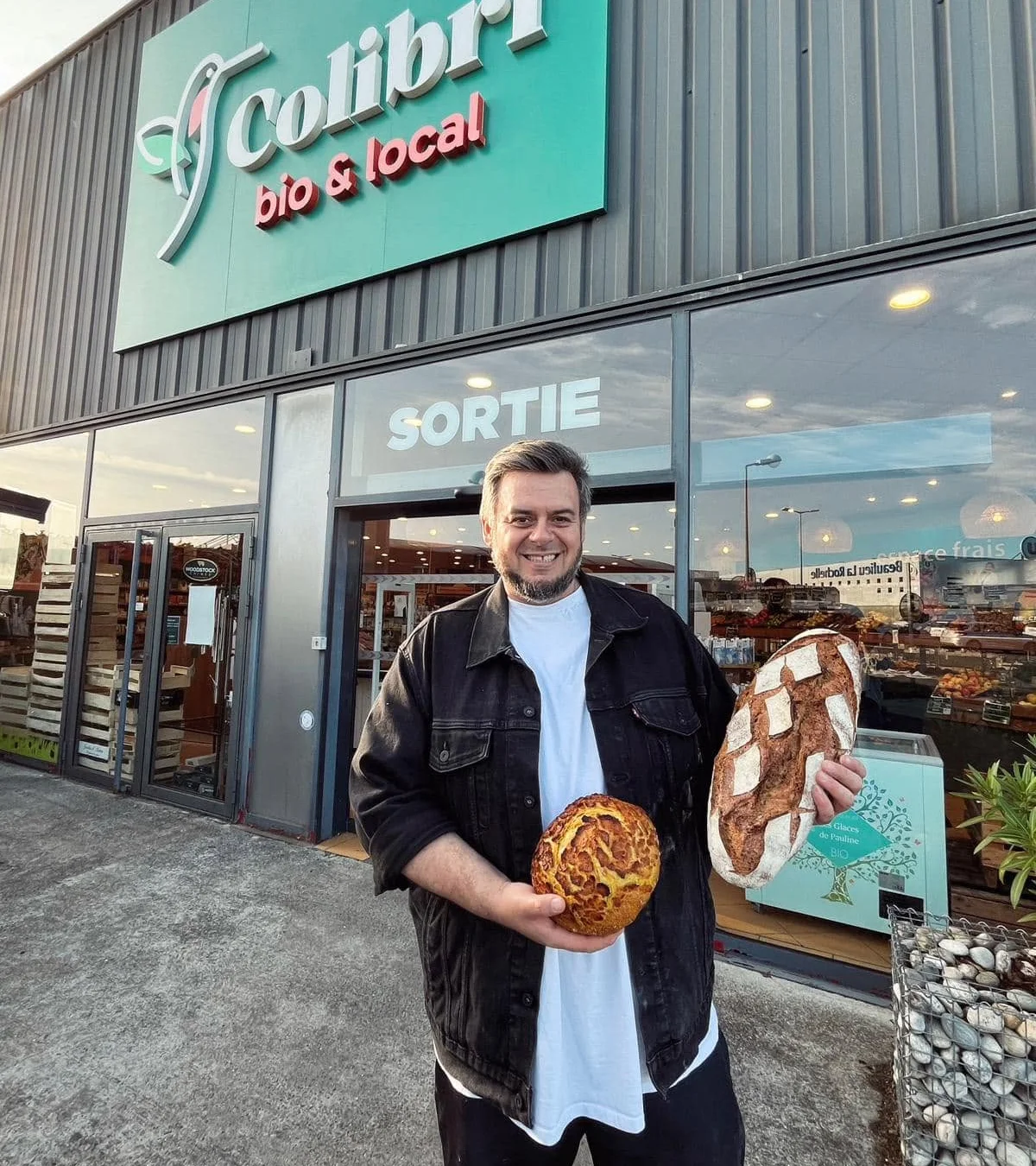 Florent Rocher, de Pain Nature, avec deux de ses pains au levain devant un magasin Colibri